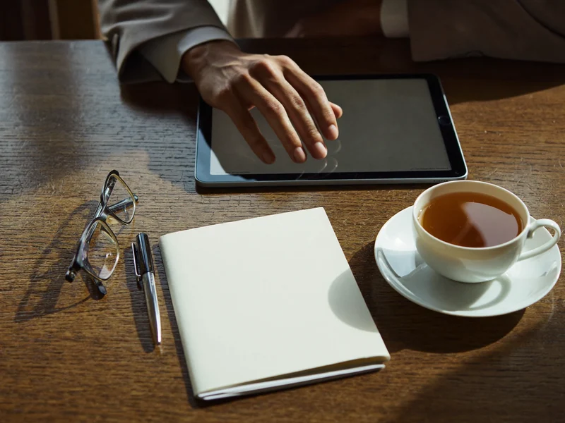Illustration: Tisch mit Tablet, Lesebrille, leerem Notizblock, Stift und einer Tasse Tee.